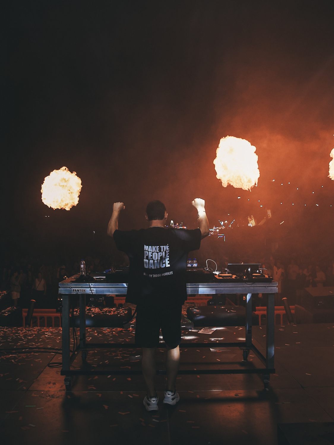 DJ Diego Morales de costas, de braços no ar, diante do público e do fogo